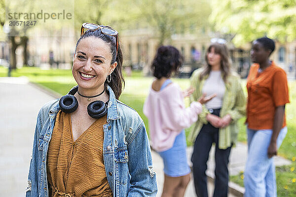 Happy woman with wireless headphones standing in front of friends