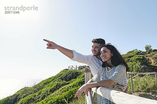 Man pointing by girlfriend standing near railing