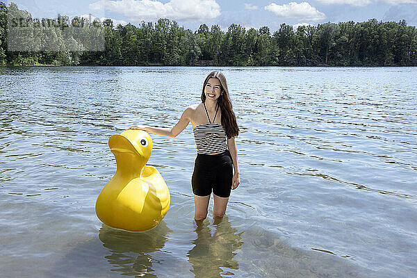 Happy girl standing with yellow rubber duck in lake