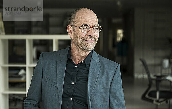 Confident mature businessman with stubble wearing eyeglasses looking away in office