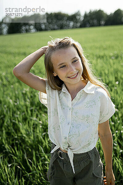 Smiling girl with hand in hair standing in field