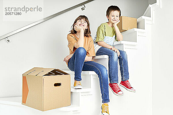 Smiling boy and girl sitting with boxes on staircase