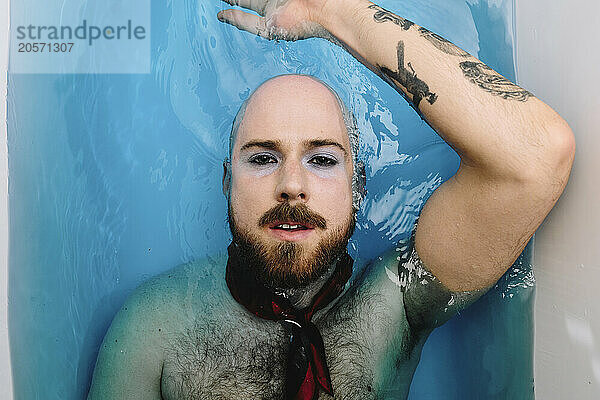 Gay man with necktie lying in bathtub