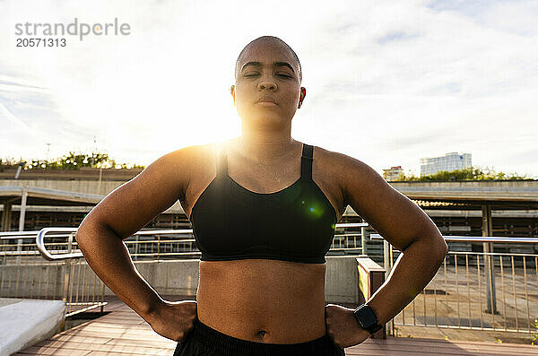 Muscular woman standing with eyes closed and hands on hip under sky