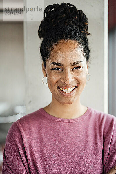 Happy businesswoman with hair bun in front of column at office