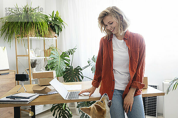 Smiling freelancer looking at dog with laptop at desk in home office