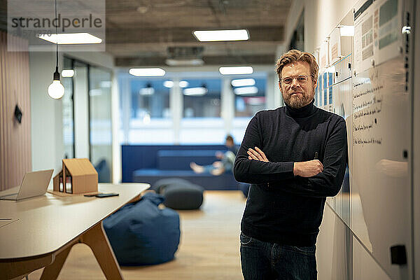 Businessman leaning with arms crossed on whiteboard at office