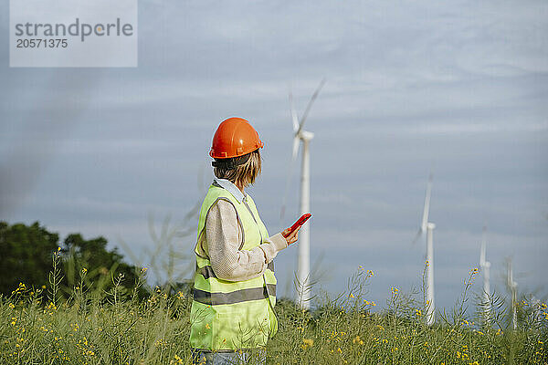 Engineer holding smart phone and looking at wind turbine