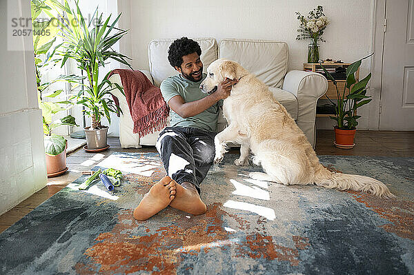 Smiling man spending leisure time with dog sitting on carpet in living room at home