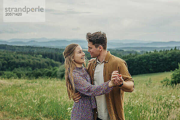 Smiling young couple dancing in meadow on mountain