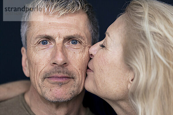 Blond senior woman kissing man on cheek against black background