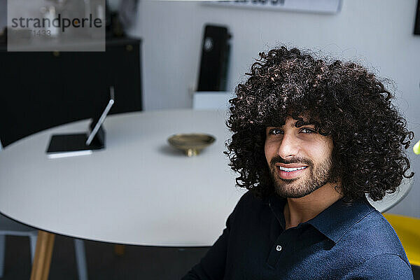 Smiling young businessman with curly hair and stubble sitting at office