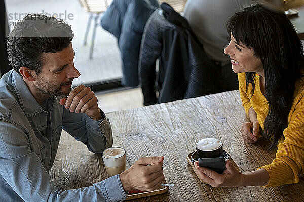 Happy businessman discussing with colleague at table in cafe