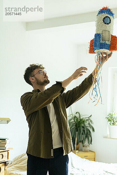 Young man with rocketship shaped pinata in bedroom at home