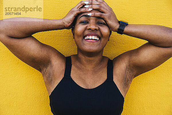 Happy bald woman with head in hands leaning on yellow wall