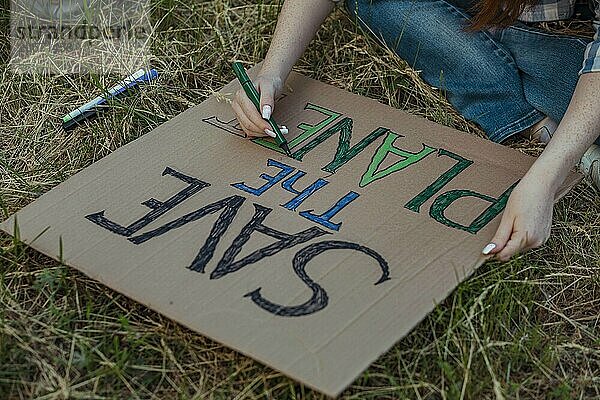 Hands of girl coloring alphabets of protest banner at public park