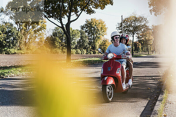 Happy young couple riding motor scooter at country road