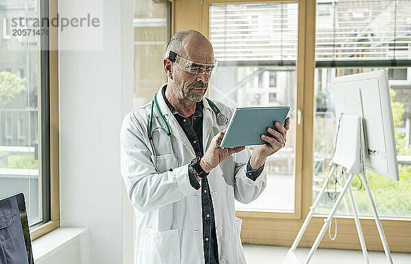 Confident mature doctor wearing smart glasses using tablet PC at hospital