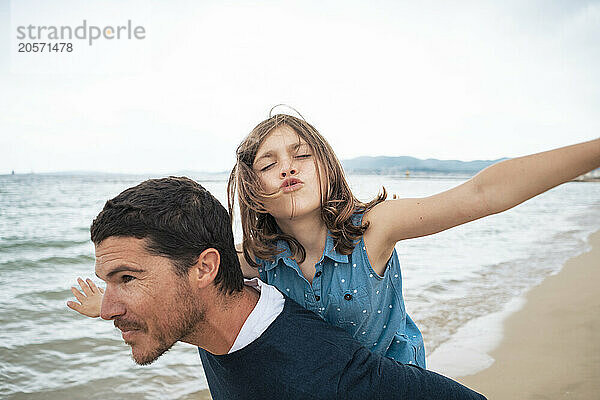 Smiling father giving piggyback ride to daughter at beach