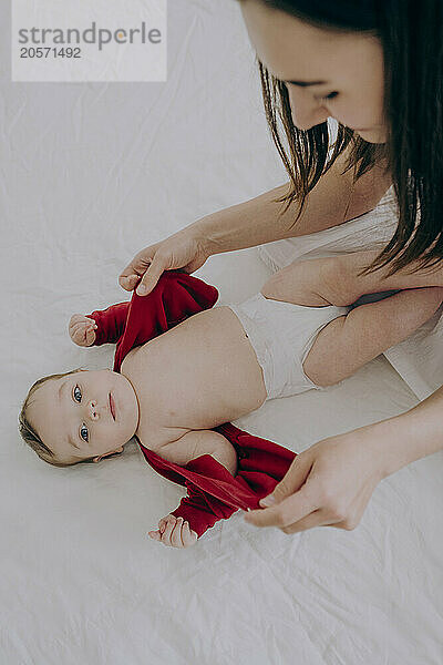 Mother changing son's clothes lying on bed at home