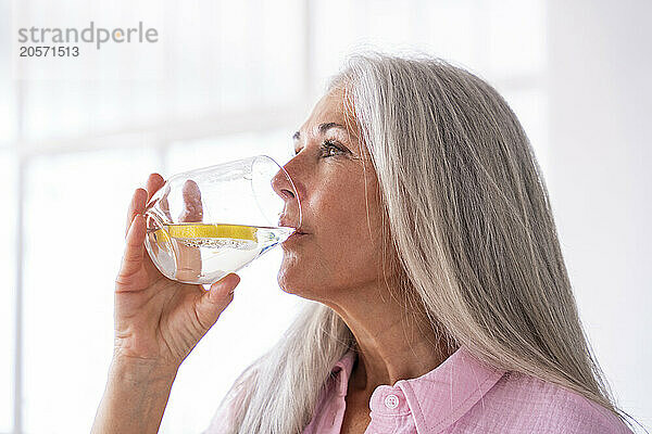 Thoughtful woman with gray hair drinking detox water at home