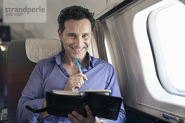 Smiling mature businessman with diary sitting in airplane