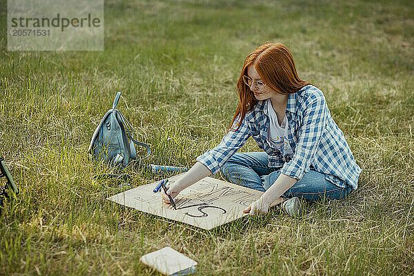 Redhead girl making protest banner sitting on grass at park