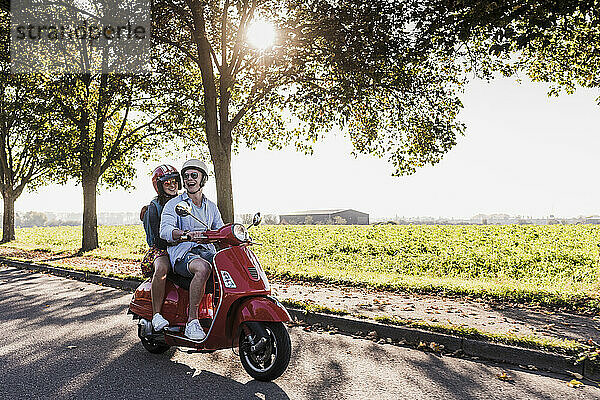 Cheerful young man riding motor scooter with girlfriend at country road