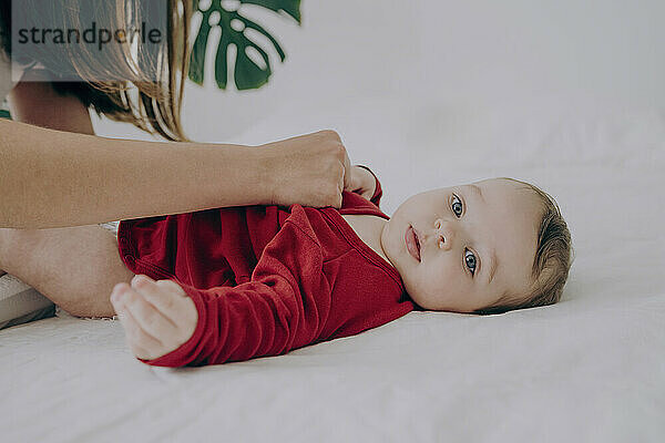 Baby boy lying on bed getting clothes changed by mother at home