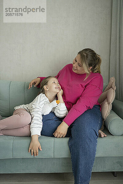 Mother sitting with daughter on sofa at home