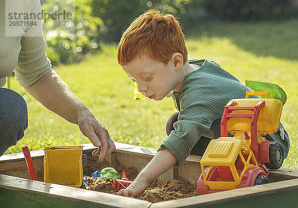 Grandmother playing with grandson in sandbox on sunny day