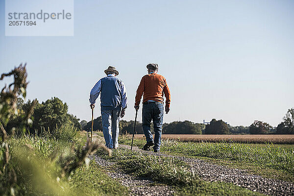 Friends walking on dirt road at field on sunny day