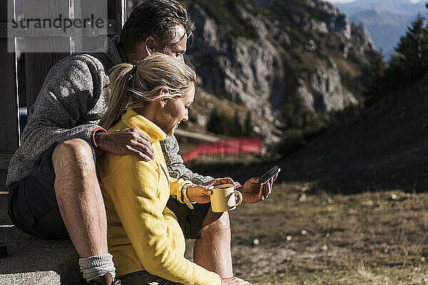 Blond hair woman with coffee cup sitting with boyfriend using smart phone