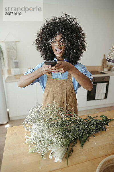 Woman photographing bouquet on table at home