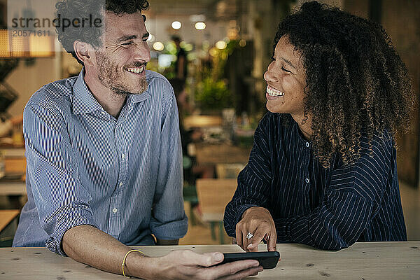 Smiling couple using smartphone and sitting in cafe