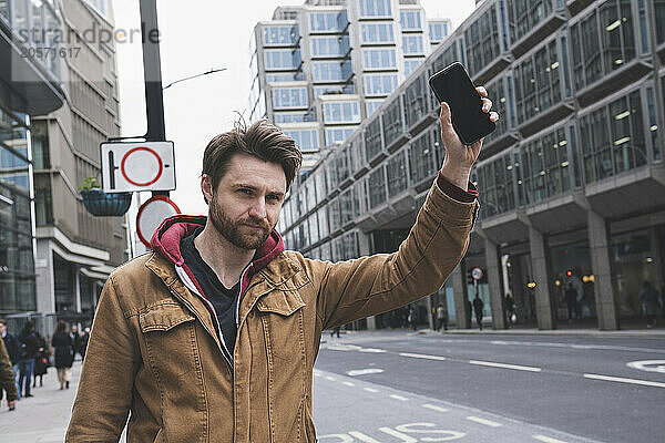 Man holding smart phone and hailing for ride at street