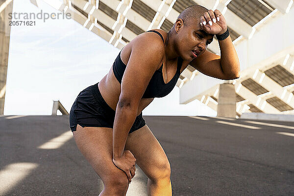 Exhausted sporty woman with hand on knee at road