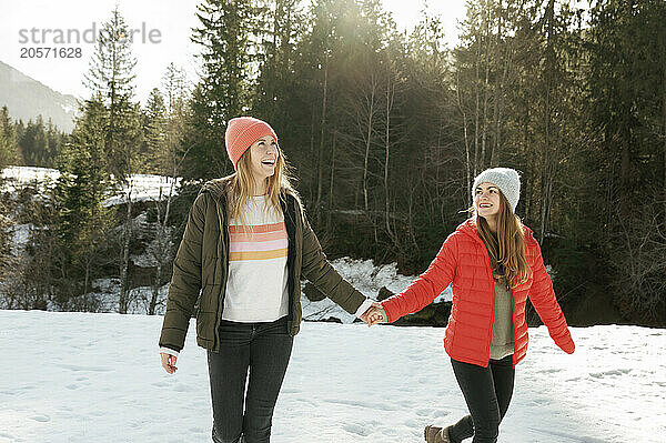 Carefree friends holding hands running on snow field