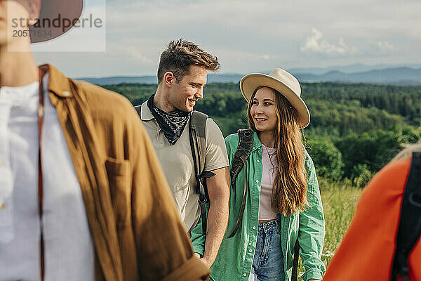 Happy couple holding hands and hiking with friends on mountain in Poland