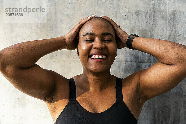 Happy muscular woman with head in hands in front of wall