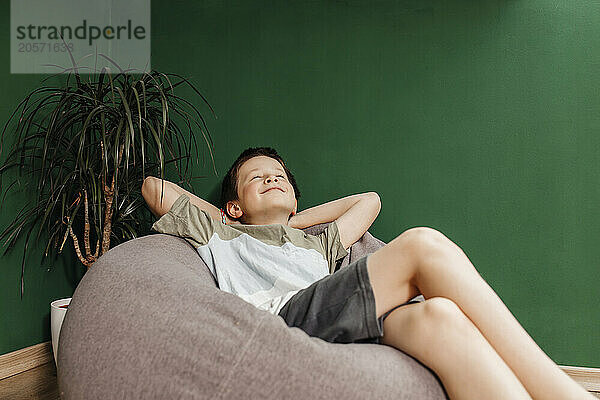 Smiling boy with eyes closed relaxing on bean bag at home