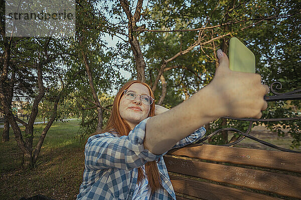 Smiling teenage girl taking selfie through smart phone at public park