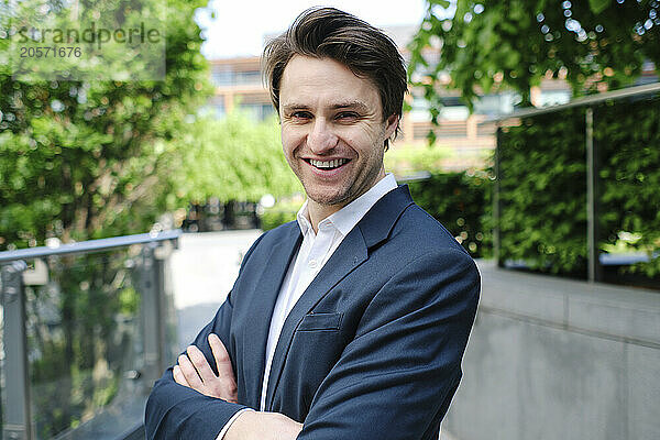 Happy businessman with arms crossed standing in office park