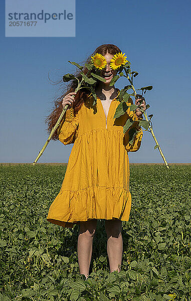 Teenage girl with red hair in a yellow dress holding sunflowers in a green field