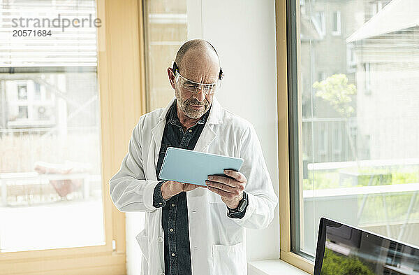 Confident mature doctor wearing smart glasses using tablet PC at clinic