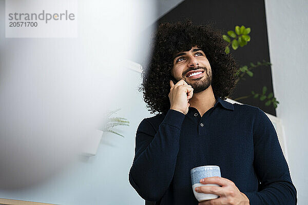 Smiling businessman talking on mobile phone standing with coffee cup at office