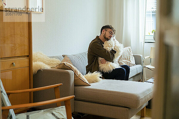 Relaxed young man hugging fake fur cushion sitting on sofa at home