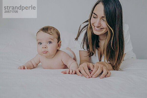 Happy mother lying on front with baby boy in bed at home