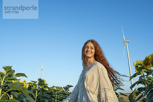 Teenage girl with red hair in sunflowers field and wind generators in the horizon