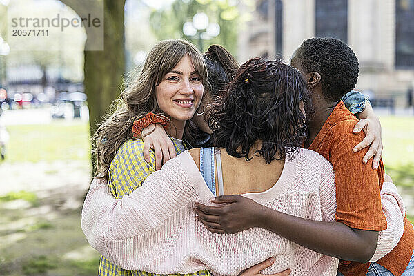 Smiling young woman huddling with multiracial friends at park